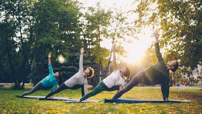 People practicing yoga in a park at sunset